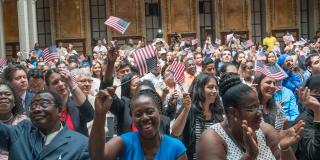 Photograph of new citizens waving small American flags at a ceremony in the Stephen A. Schwarzman Building