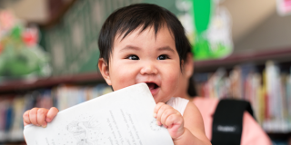 A happy baby holding a book near its mouth