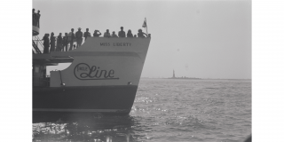 Historic photo of the Circle Line ferry filled with tourists in the foreground with the Statue of Liberty in the background