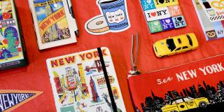 Photo of red tablecloth with various NYC-related merchandise arranged neatly, including a toy cab, stickers, notebooks, and more
