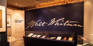 photograph of back wall of exhibition, wall is dark blue and walt whitman signature is in white across wall