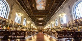 Interior photograph of the Rose Main Reading Room which features an ornate mural on the ceiling, dark wood bookshelves and many rows of tables for researchers