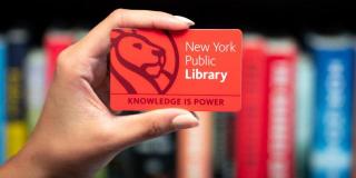 Hand holding a red NYPL library card that reads: New York Public Library, Knowledge Is Power