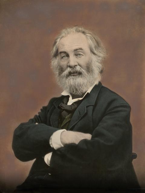 hand-colored photograph portrait of an older Walt Whitman with his arms crossed in front of him, white beard, and dark bluegreen suit