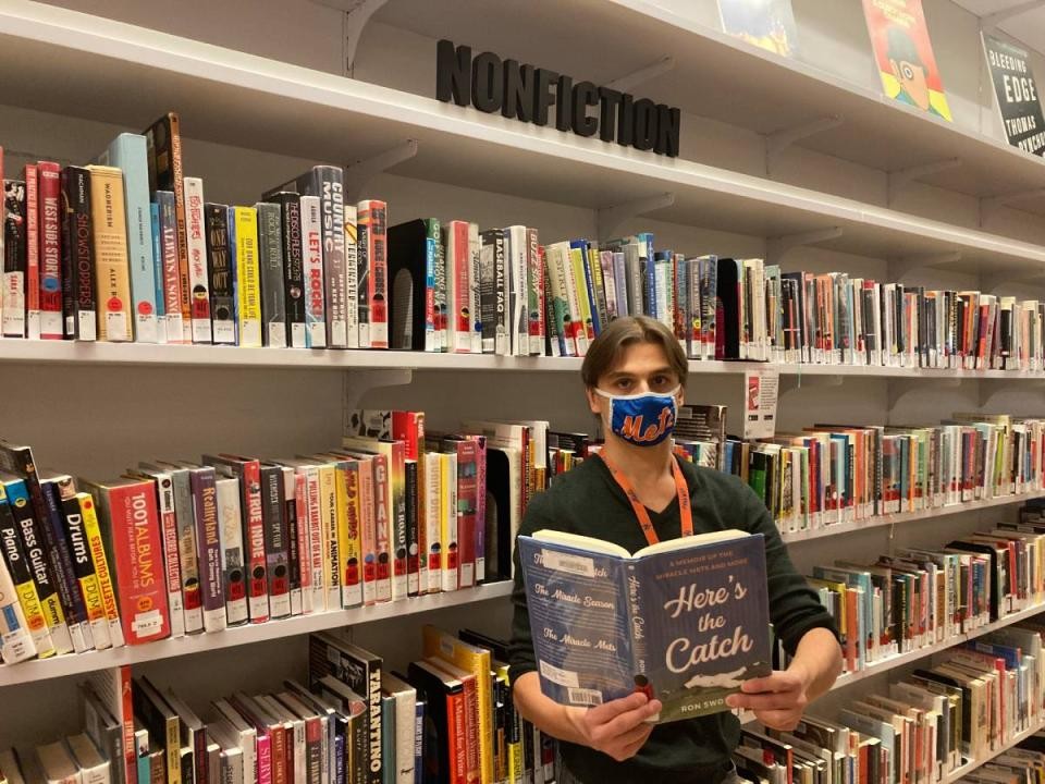 library staff member holding book about baseball in front of shelves