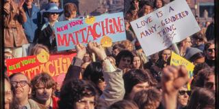 Color photo of men and women holding signs at a demonstration. The signs read "Love is a many-gendered thing" and "New York Mattachine"