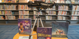 Photo of an NYPL Stargazing Kit spread out on a table with items including: a travel telescope and three books