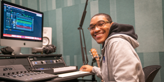Photo of a smiling teenager in the recording studio booth at the Teen Center at SNFL. 