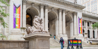A marble lion stands at the entrance of a building with columns and rainbow banners that read: Libraries Are For Everyone Stand Against Book Bans.