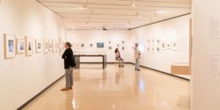 Three people in a gallery with white walls lined with images
