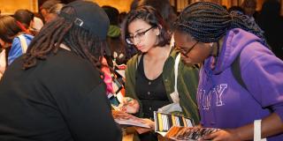 Two teens holding pamphlets and speaking to a recruiter at NYPL's college fair.